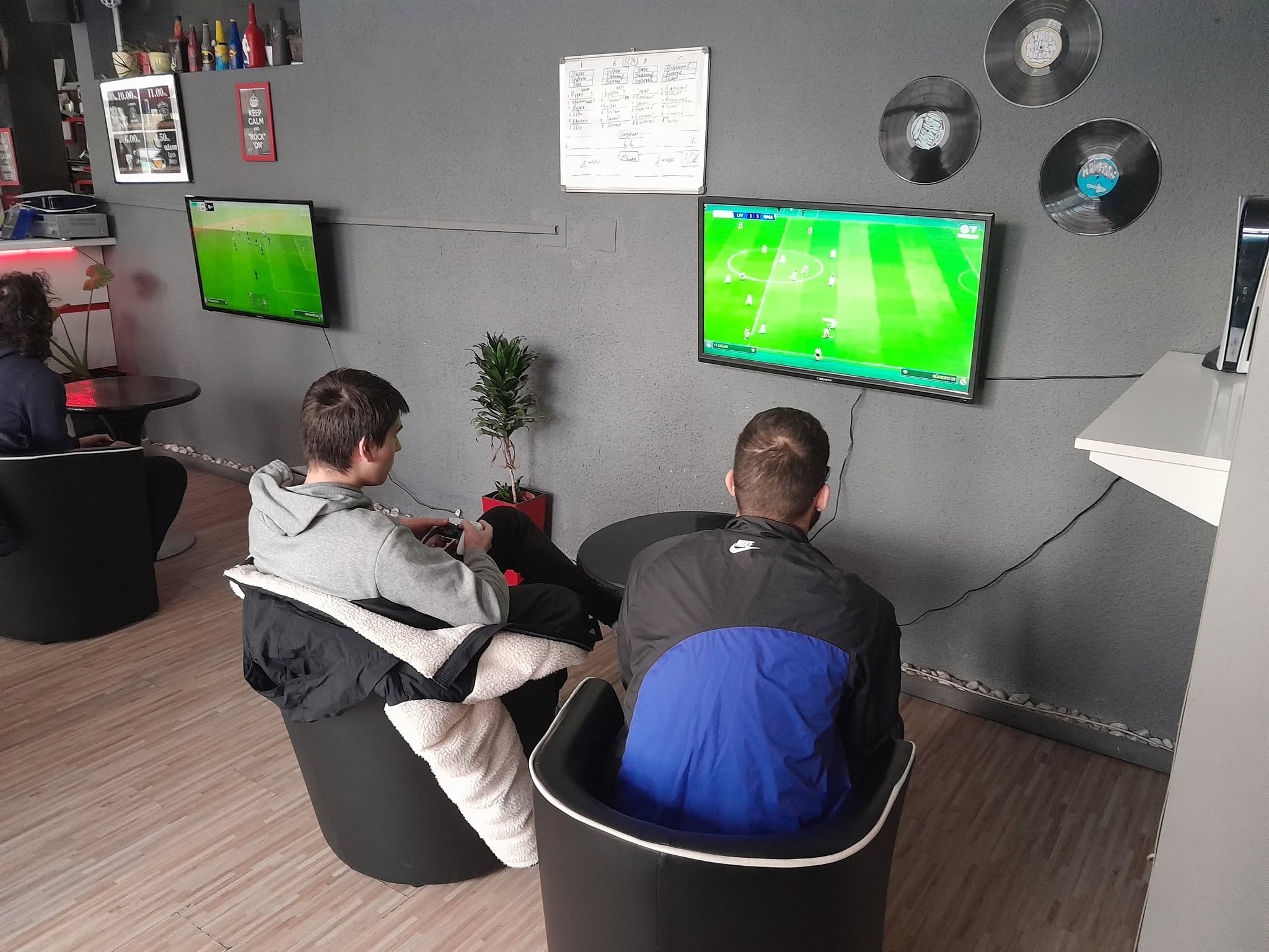 Двама души играят FIFA на конзолата пред телевизора в бара.
